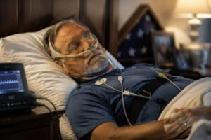 A veteran sleeping peacefully with subtle American flag elements and medical sleep monitoring equipment in soft, respectful